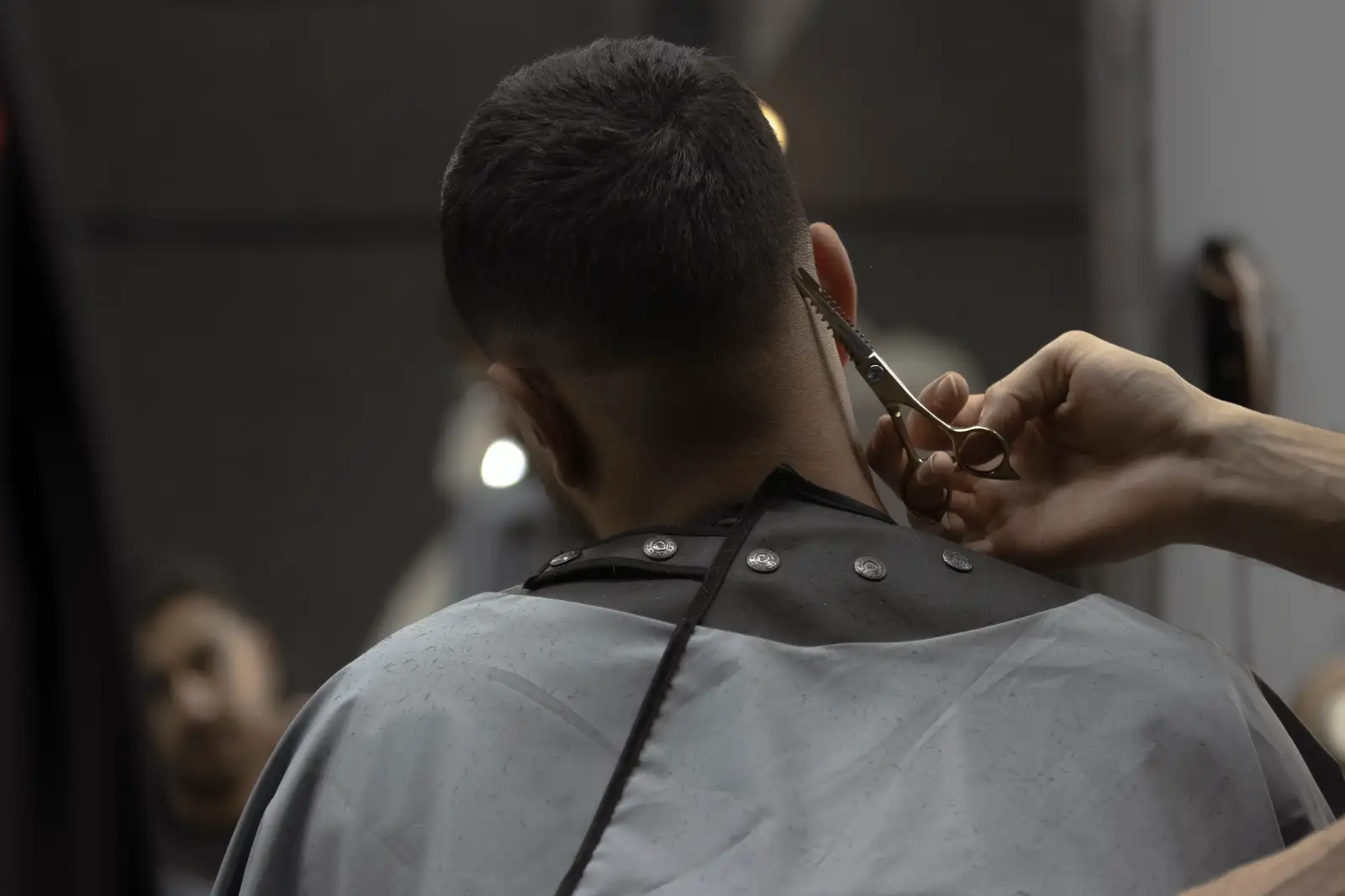 A stylist’s hands cutting the back of a client’s short dark hair with scissors